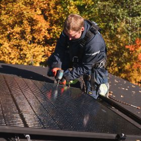 Sähkömies kiinnittää aurinkosähköpaneelia asennuskiskoon katolla.